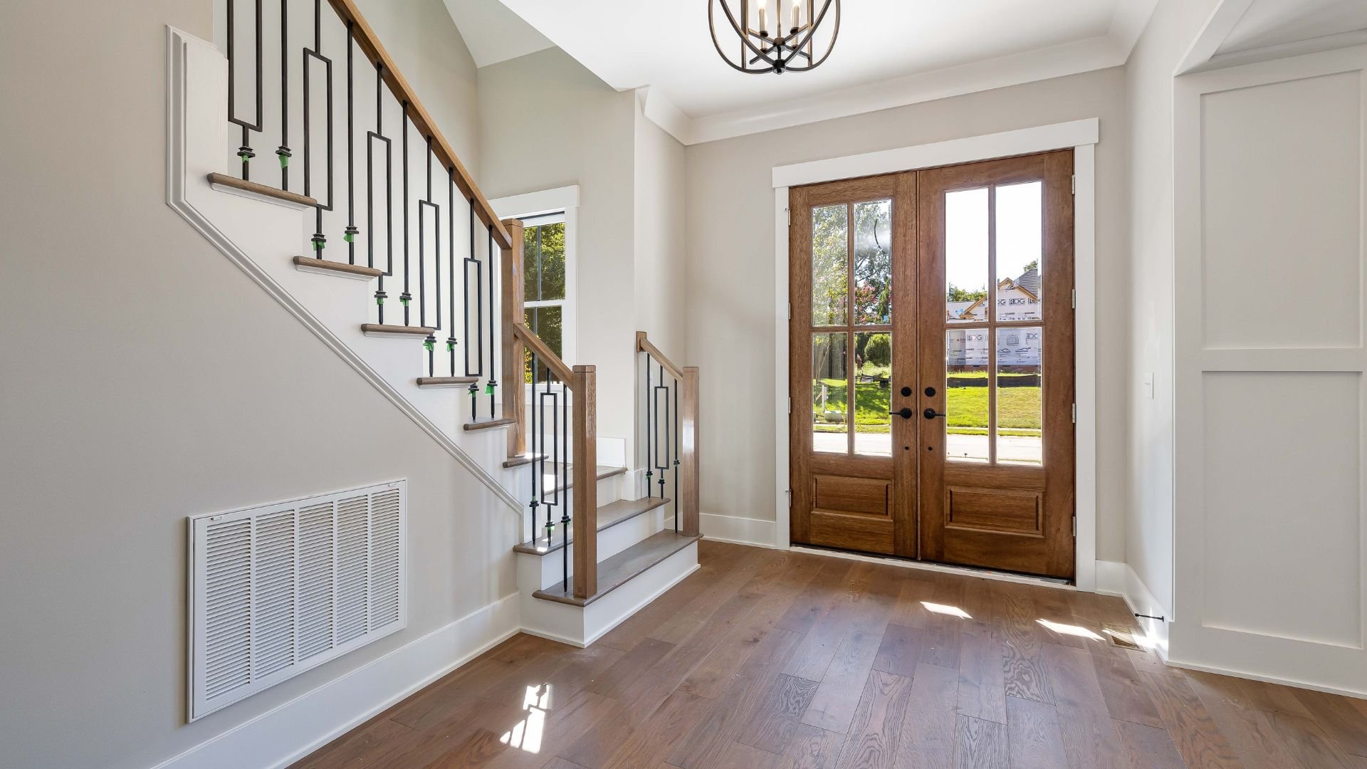 Bright entryway with wooden floor, iron staircase, and French doors