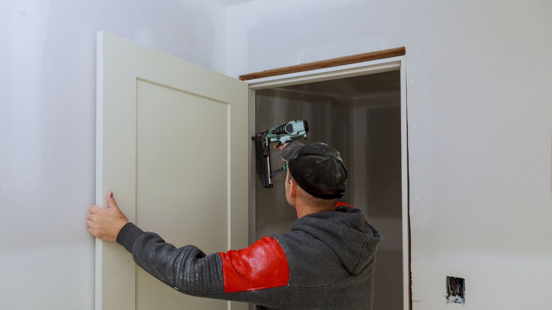 Worker installing door trim with nail gun in interior room