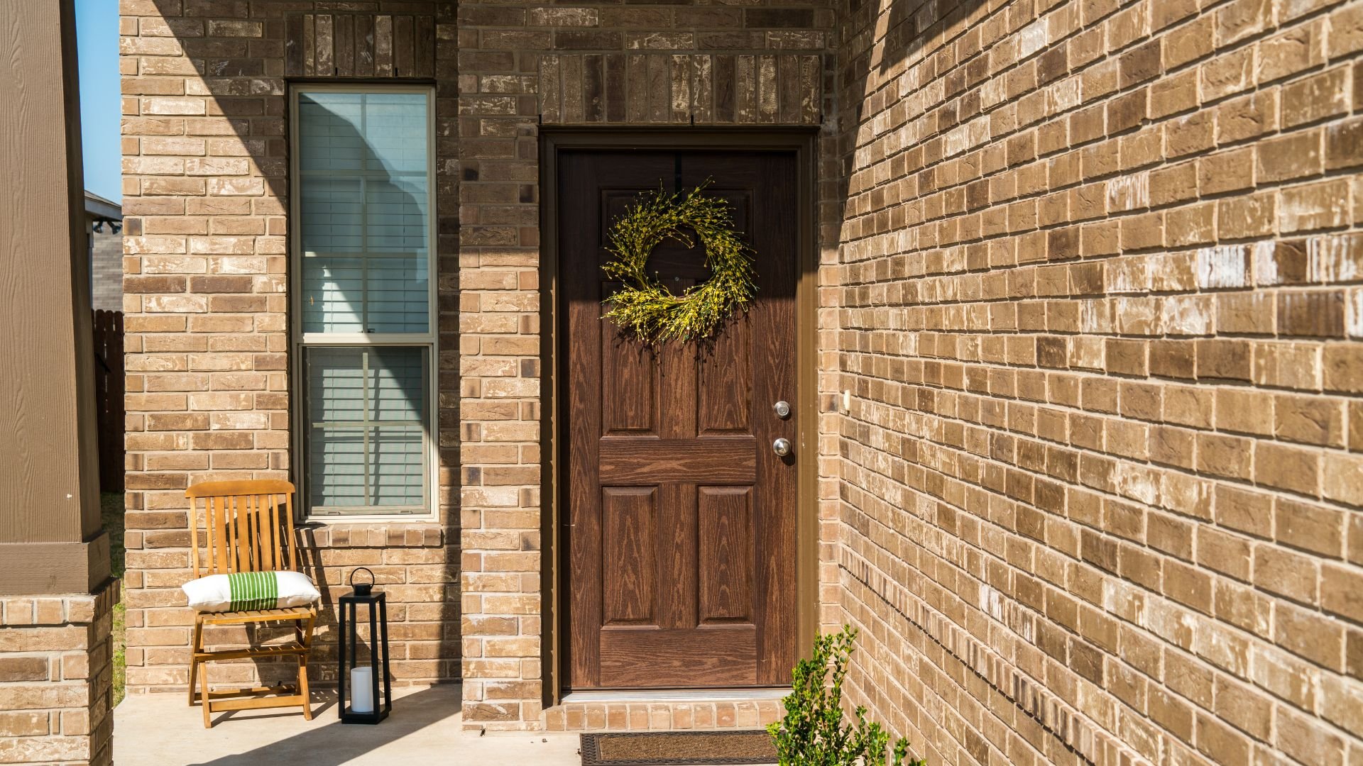 Wooden front door with yellow wreath, brick exterior, chair and lantern
