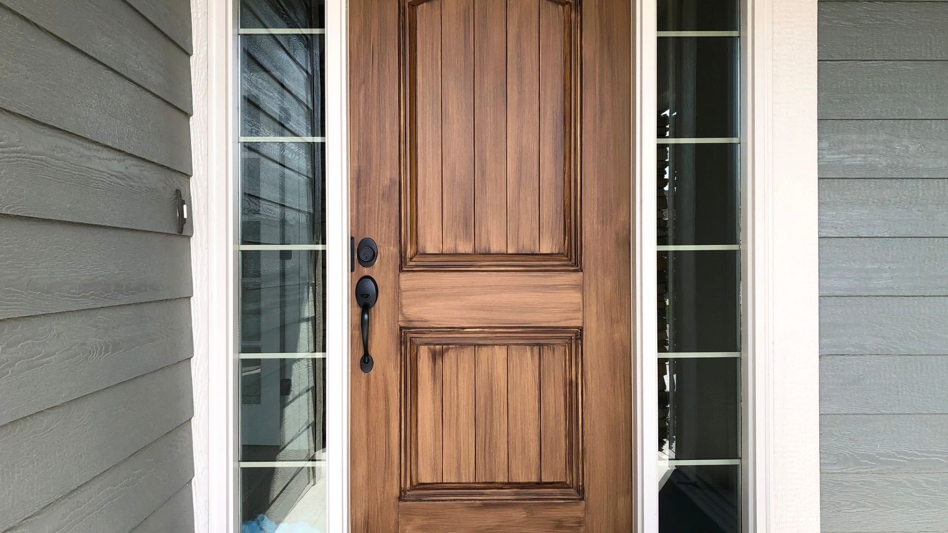 Wooden front door with black handle, flanked by glass sidelights