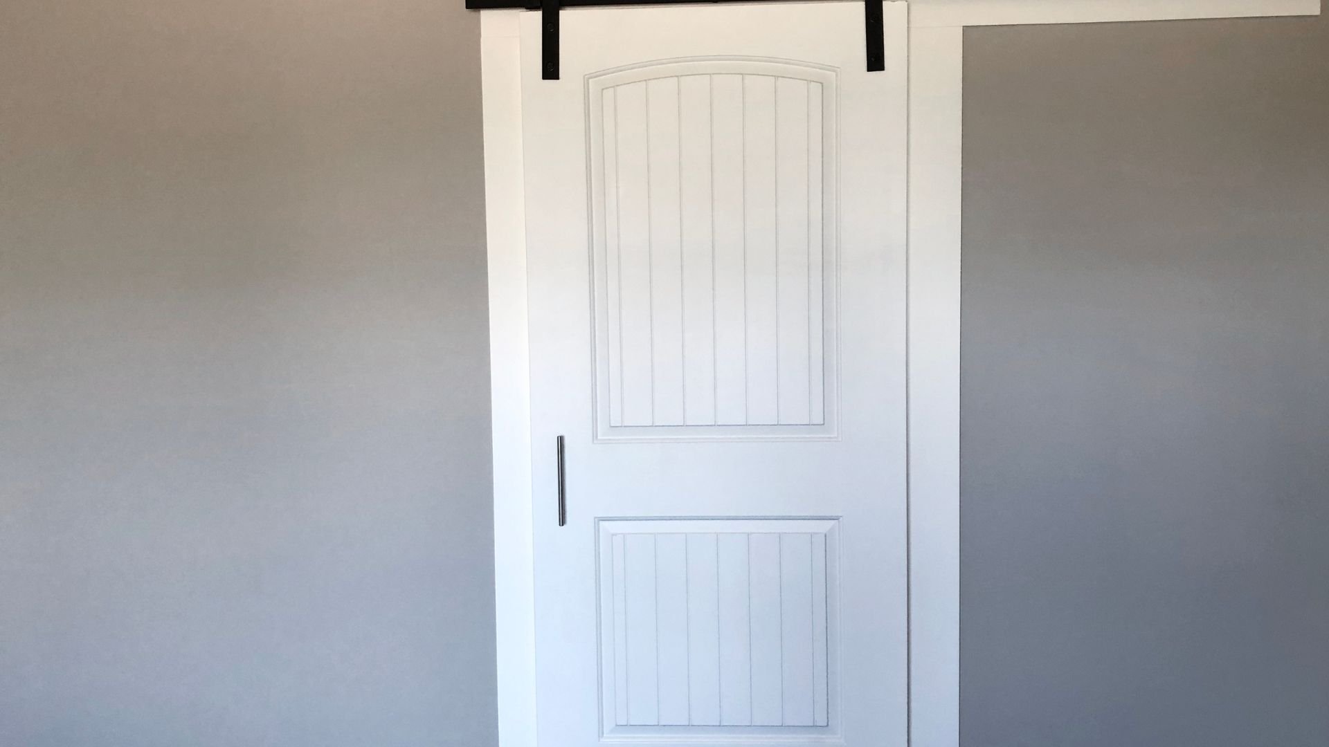 White sliding barn door with vertical panels mounted on gray wall