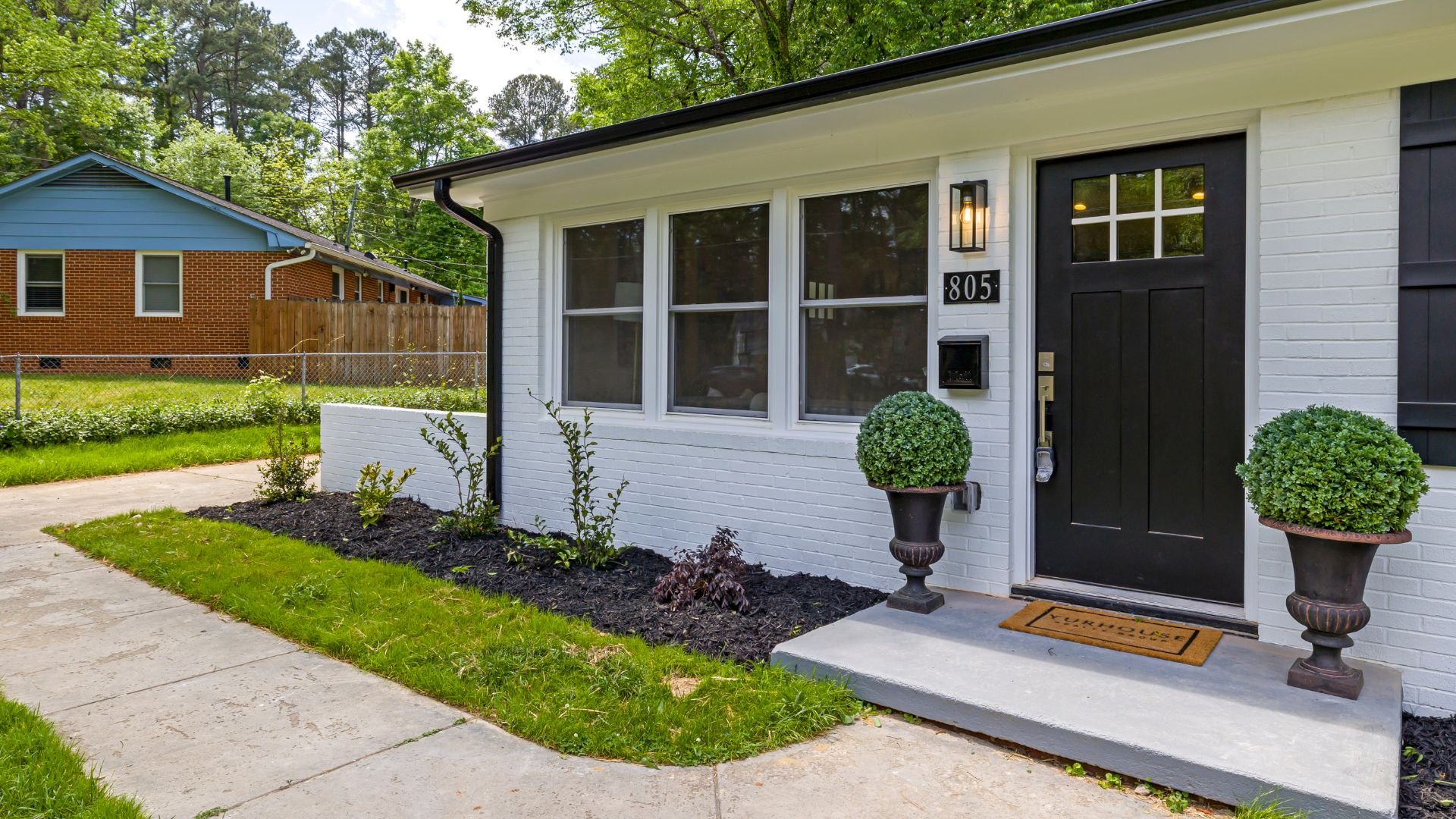 White brick house with black door, potted plants, and welcoming front entrance